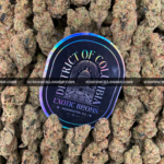 Slurricane strain cannabis buds featuring dense, deep olive-green nugs with purple hues and amber pistils, coated in frosty trichomes. This potent indica-leaning hybrid offers sweet berry, spicy earth, and blueberry tea aromas, delivering strong relaxation and couch-lock effects. Perfect for stress relief, pain management, and sleep aid.