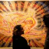 Two people viewing a psychedelic artwork by Alex Grey depicting entangled human forms with glowing energetic anatomy, often associated with DMT or spiritual visions