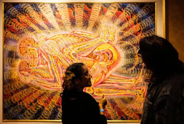 Two people viewing a psychedelic artwork by Alex Grey depicting entangled human forms with glowing energetic anatomy, often associated with DMT or spiritual visions